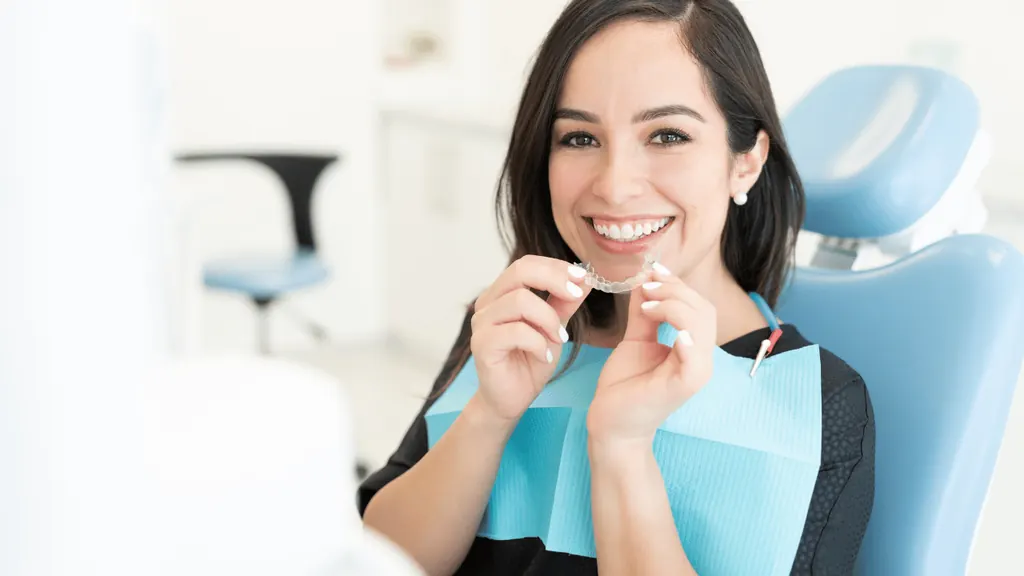 Mulher sorrindo segurando um alinhador invisível em consultório odontológico