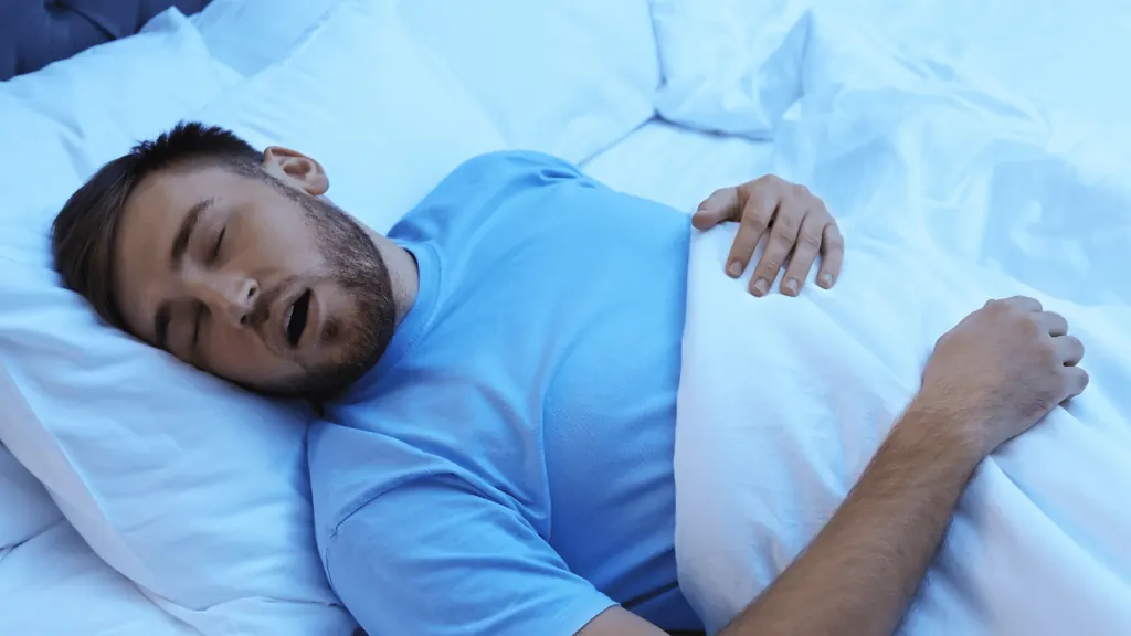 Homem dormindo com a boca aberta, sinal comum de apneia do sono associada ao bruxismo
