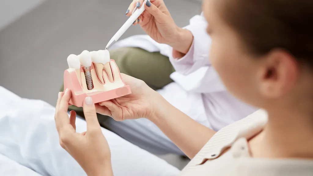 Dentista mostrando modelo anatômico de implante dentário para paciente
