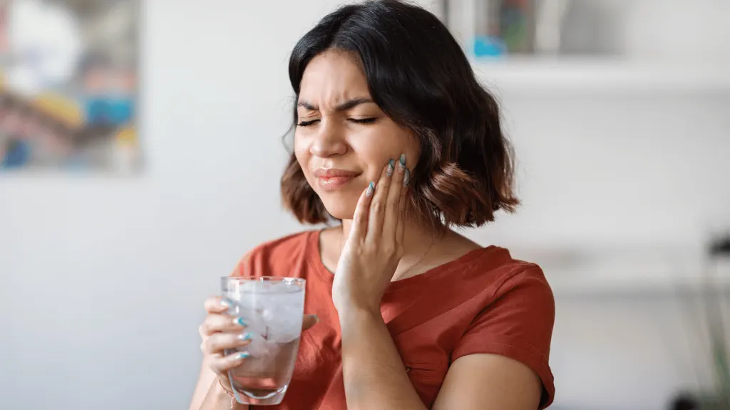 Mulher com a mão no rosto, sentindo sensibilidade nos dentes após o clareamento dental
